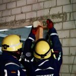 Zwei Personen in Einsatzbekleidung des THW verkeilen zwei Kanthölzer in einer Türöffnung.